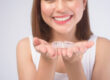 Young smiling woman holding invisalign braces over white background studio.