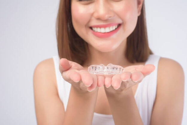Young smiling woman holding invisalign braces over white background studio.