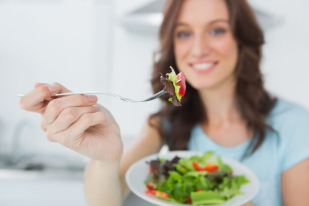Woman eating healthy salad in her kitchen.