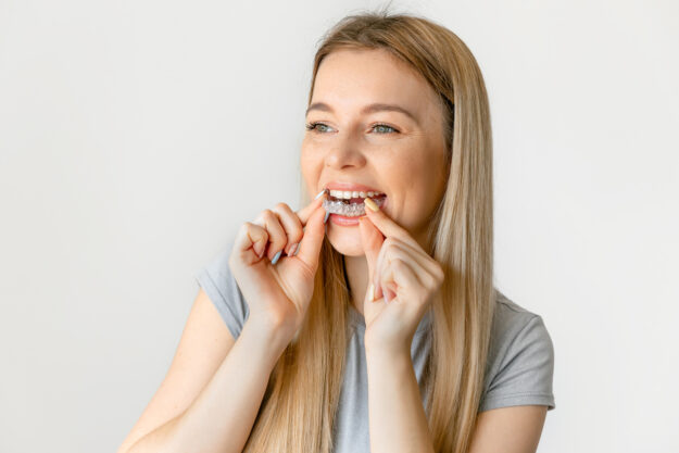 Dental care. Smiling woman with healthy teeth using removable clear braces aligner, orthodontic silicone trainer.